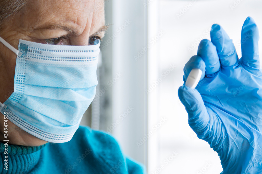 Fototapeta premium senior woman with mask and medical gloves holding pill in hand