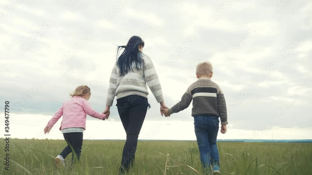 happy family. mom and little children walk in the park teamwork outdoors holding hands. woman and little boy and girl walk on a green field at sunset lifestyle happy family. mom and little children walk in the park teamwork outdoors holding hands. woman and little boy and girl walk on a green field at sunset lifestyle