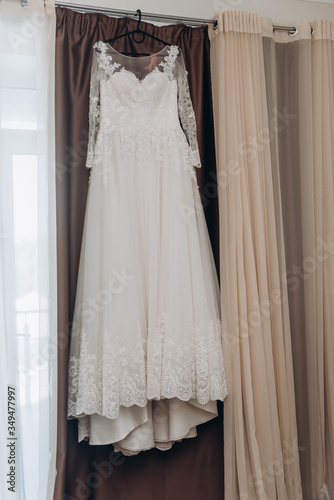 The bride's dress hangs on the window. A gentle bouquet of the bride and women's shoes stand on the windowsill