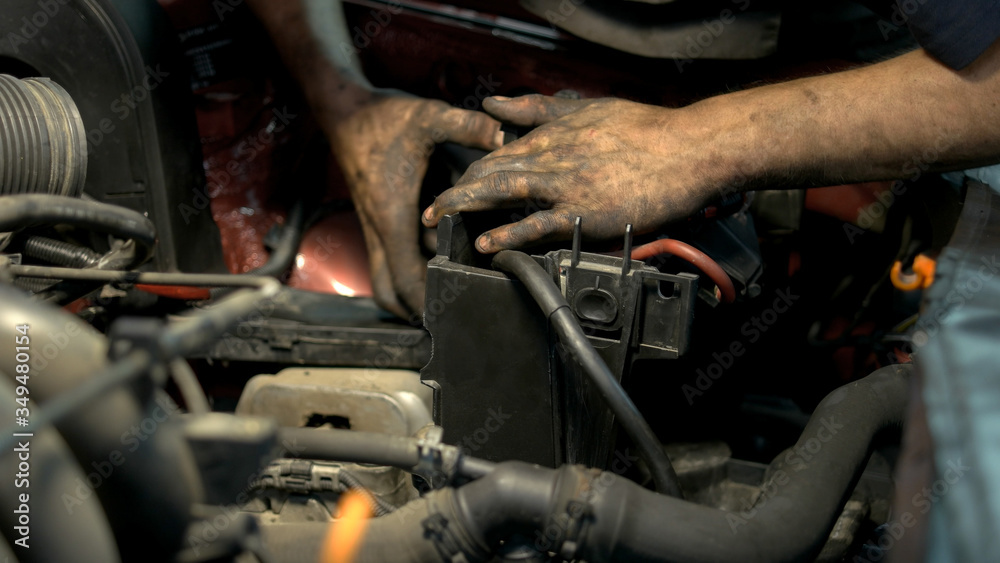 Fototapeta premium Mechanic with dirty hands uninstalling and fixing car engine details. Professinal repairman in a car service center repairing a car motor.