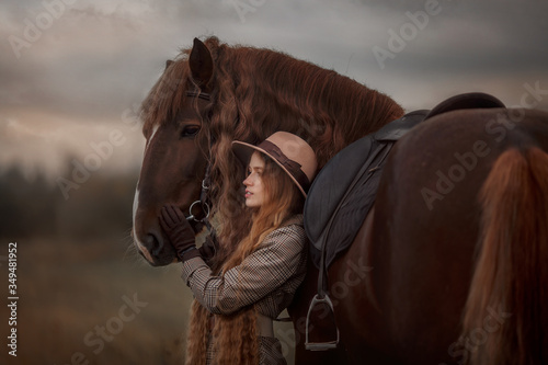 Beautiful long-haired blonde young woman in English style with red draft horse in autumn forest © Julia Shepeleva