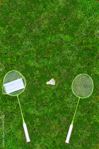 Coronavirus protection sing. Badminton rackets and shuttlecock on green grass. Medical mask on one racket. view from above