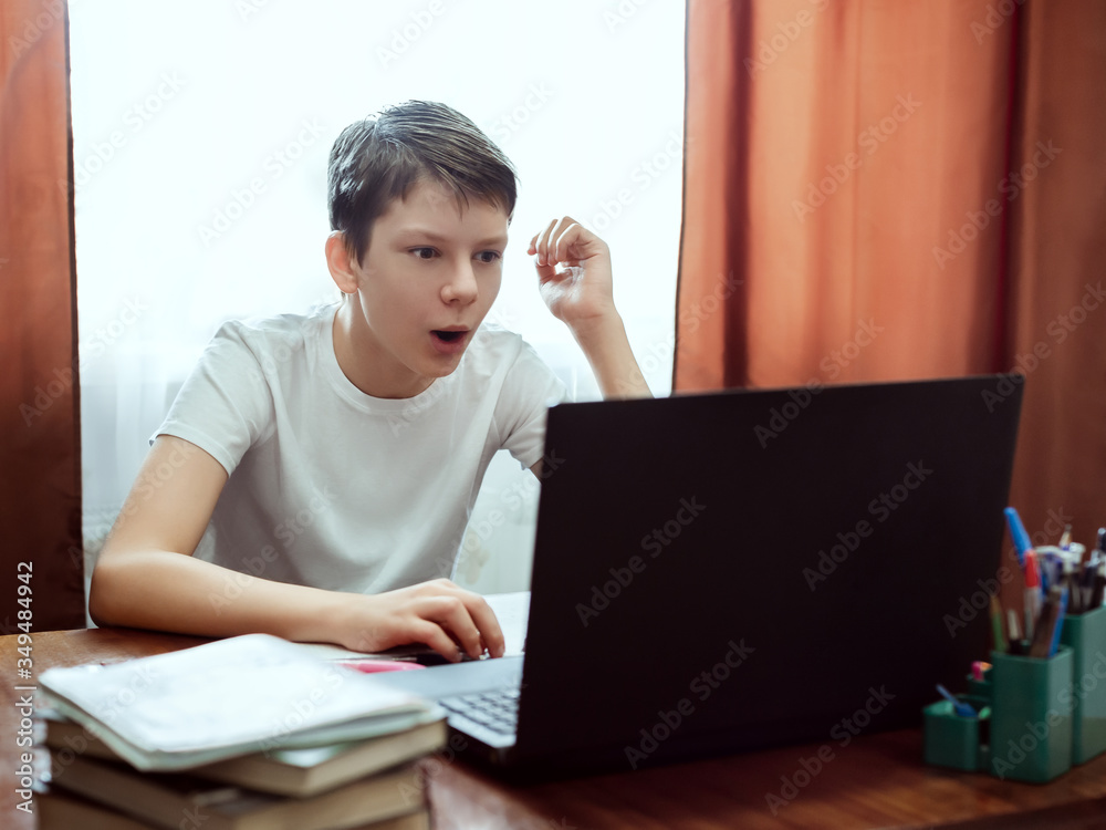 Surprised student looking at computer, watching online education classes at home. Schoolboy studying with laptop and doing school homework. Distance and e-learning education concept, online lessons Surprised student looking at computer, watching online education classes at home. Schoolboy studying with laptop and doing school homework. Distance and e-learning education concept, online lessons
