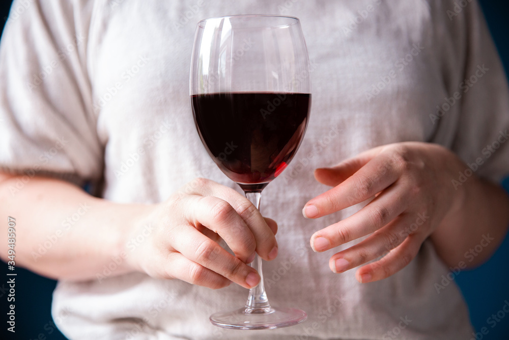 Portrait of a young woman with a glass of red wine in her hand against blue wall,