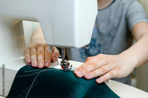 Teenager, boy learns to sew on a sewing machine at home, hands close-up. Concept - hobbies - unisex, training, new skills