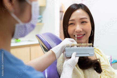 dentist using tooth color chart to compare with teeth of asian woman patient preparing for laser tooth whitening in dental clinic. dentistry and healthcare concept