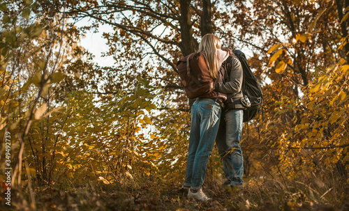 Kiss of backpackers in love hugging while standing alone against the backdrop of autumn forest outdoors © Svyatoslav Lypynskyy