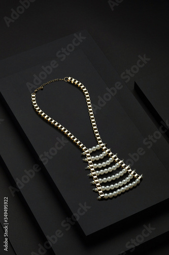 Subject shot of a fashion choker made as a golden track chain with a breastplate of pearl beads and rhinestone. The carcanet is located on the stepped platform with black fabric surface. photo