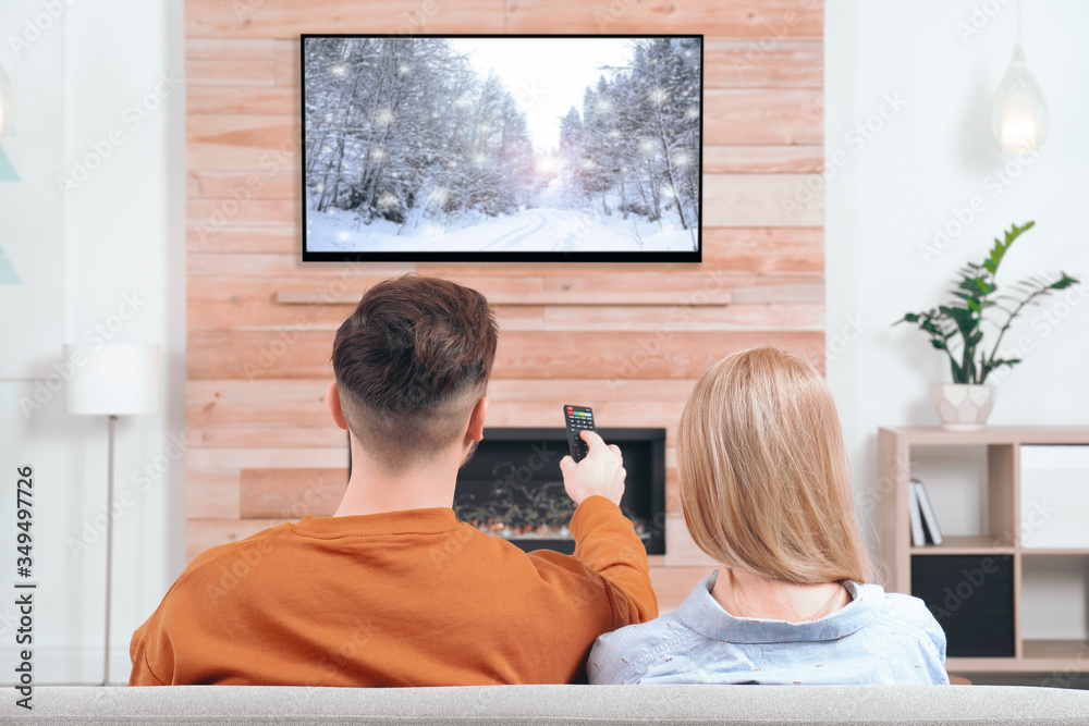 Φωτογραφία Couple watching TV on sofa in living room with decorative fireplace