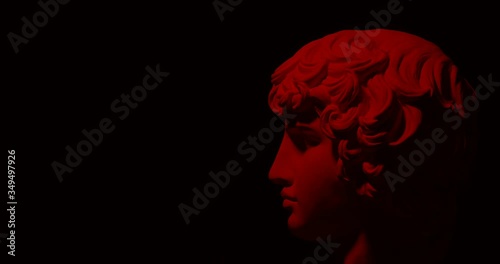Epic studio shot of rotating gypsum head with moving and changing red lighting. The play of light and shadow on half the face of statue of man. On black background isolated 4k