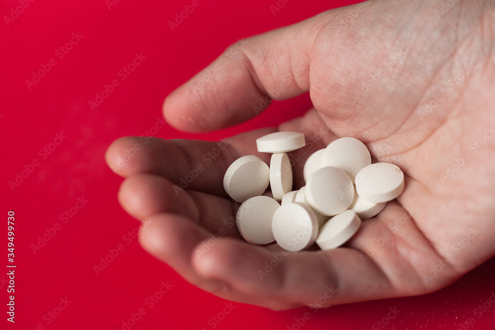 Hand of woman holding white pills. Vitamins in woman's hand. Isolated on red background. Hand of woman holding white pills. Vitamins in woman's hand. Isolated on red background.