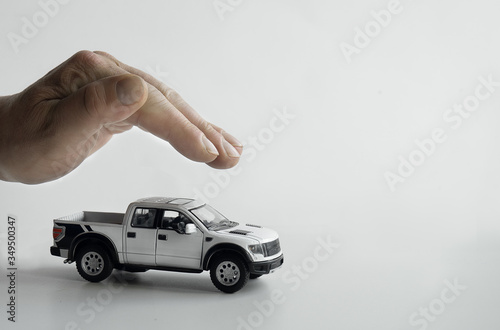 Male hand in a protective gesture, holding hand over a toy car on a white background.