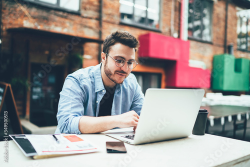 Young man sitting at table on street and working on laptop