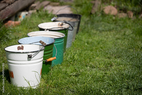 Many different buckets stand in a row to collect rainwater. Buckets of water stand on the grass in the garden next to the house. Village concept. Copy space