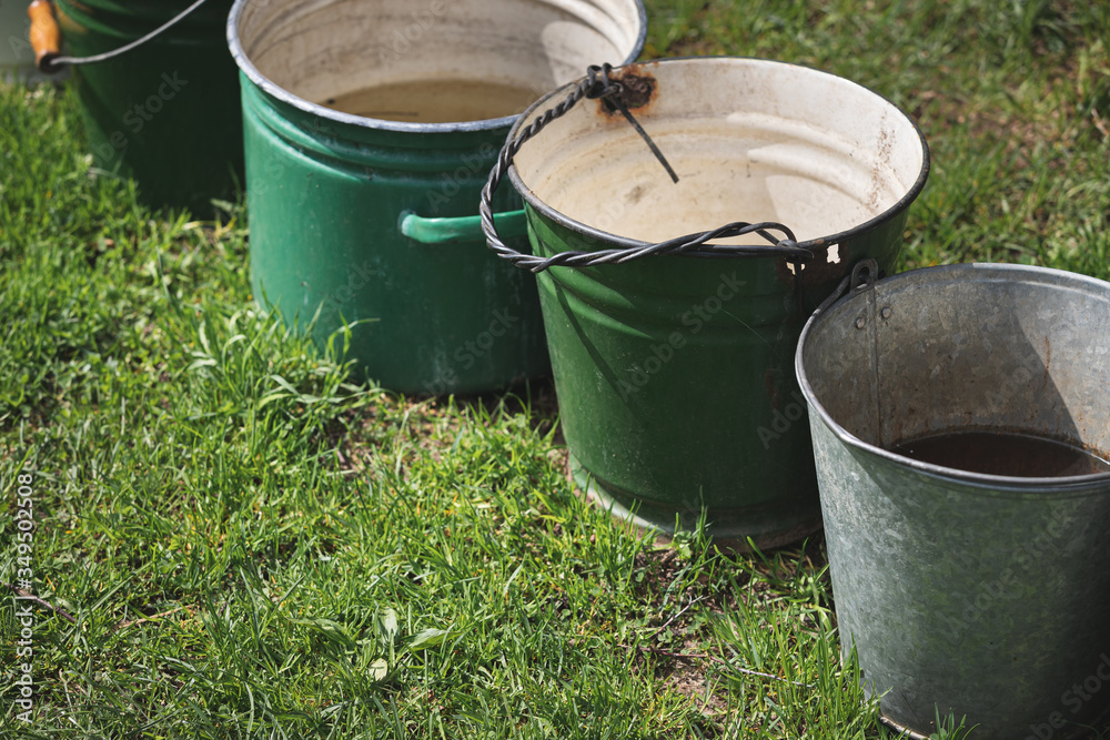 Top view on buckets with rainwater stand on green grass. Close-up of old buckets standing in one line. Top view on buckets with rainwater stand on green grass. Close-up of old buckets standing in one line.