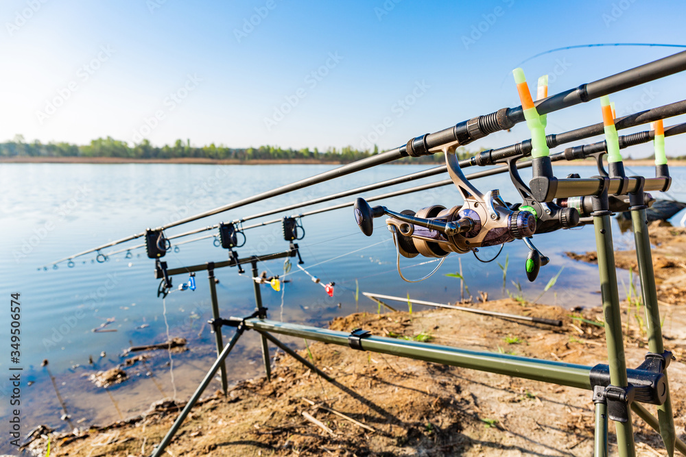 Fishing rods set for carp up on holder with bite alarms and illuminated indicators . Professional fishing equipment Fishing on the shore of a quiet clean lake on a warm summer silence morning. Fishing rods set for carp up on holder with bite alarms and illuminated indicators . Professional fishing equipment Fishing on the shore of a quiet clean lake on a warm summer silence morning.