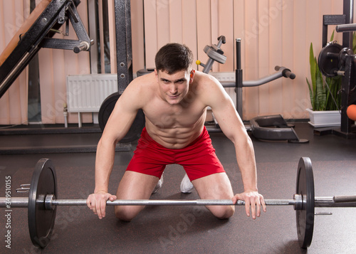 Young man flexing muscles with barbell in gym.