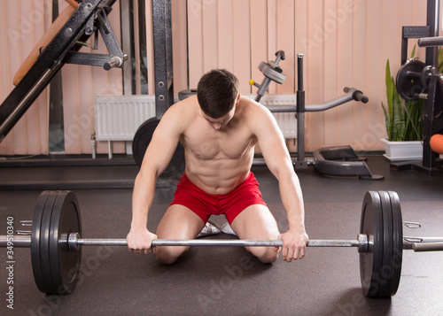 Young man flexing muscles with barbell in gym.