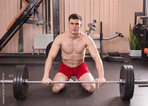 Young man flexing muscles with barbell in gym.