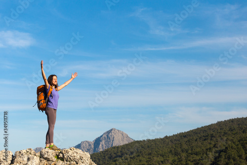 A woman with a backpack stands on top of a mountain and admires the beauty of a mountain valley.