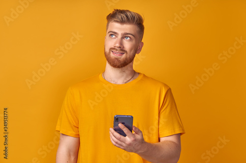 Pensive positive young caucasian guy with beard is thinking about something while holding smartphone in hands. Concept of free high-speed Internet and dream of unlimited downloads. Advertising space © antianti