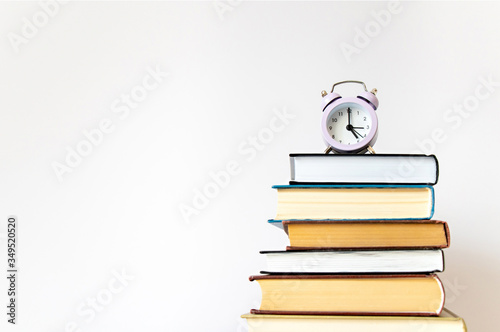 Purple small alarm clock on stack of books on white background wall with copy space. Concept of time to study, read books. Concept of preparing for exams