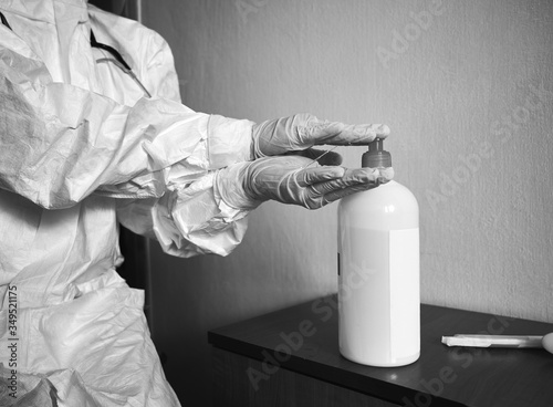 Fotografía Black and white cropped image of doctor in PPE suit, gloves, decontaminating hands with alcohol sanitizer