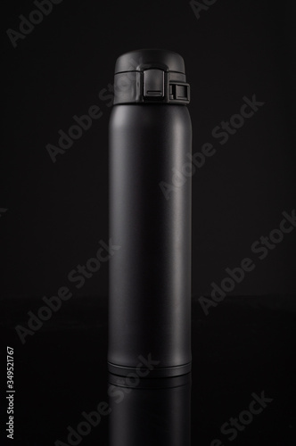 Black thermos on a black background with reflection. Thermo mug for coffee or tea. photo