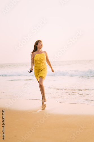 Goa, India. Young Caucasian Woman In Yellow Dress Walking On Seashore And Enjoying Life In Summer Sunlight © Grigory Bruev