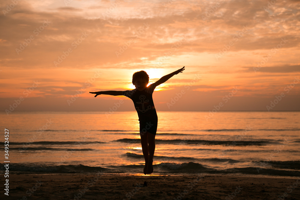 A boy jumps in the air arms to the sides at sunset on the sea