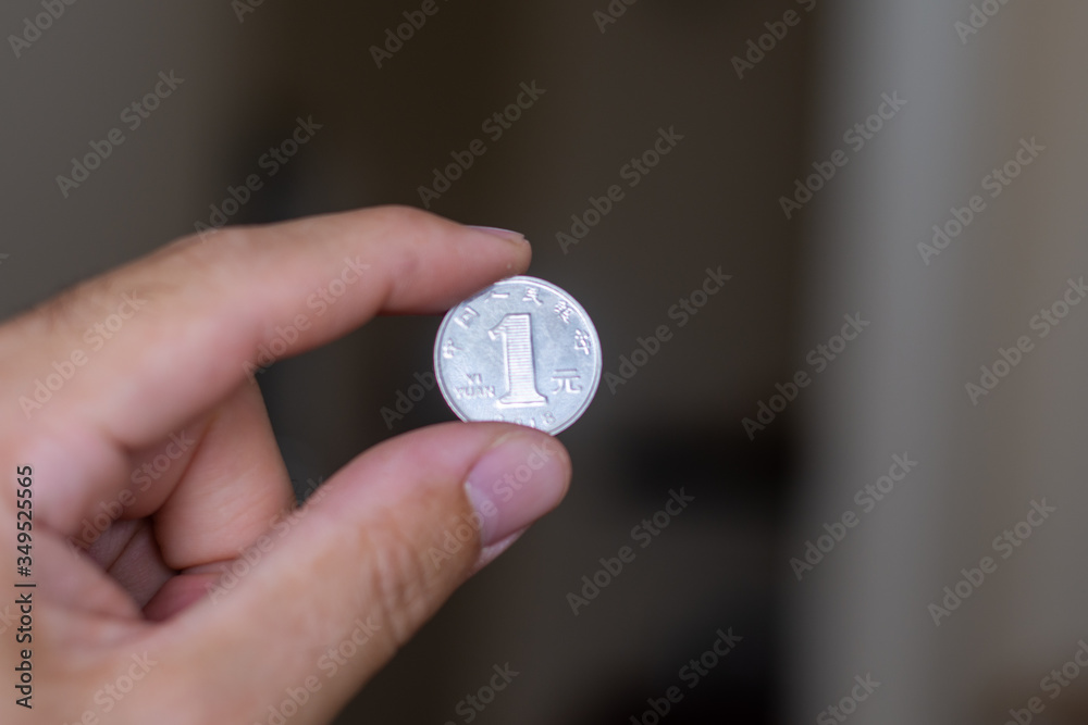 Persons hand holding out a one reminbi (RMB) or Yuan, the Currency of China - on a brown background. Money exchange.' Persons hand holding out a one reminbi (RMB) or Yuan, the Currency of China - on a brown background. Money exchange.'