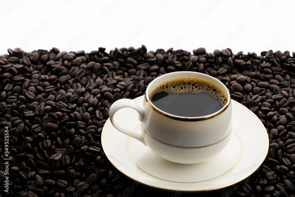 Hot black coffee with foam in a white coffee cup on coffee beans field background