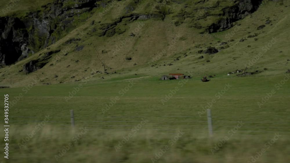 View of green meadows and a lonely house from the car window. Hills and mountains of Iceland