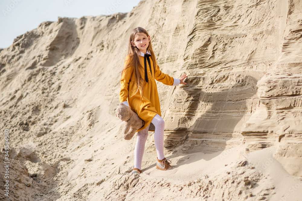 Naklejka premium young woman in a yellow dress. little girl playing on the beach. young woman with teddy bear. Girl travels with her favorite toys.
