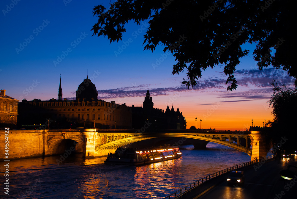 Naklejka premium Paris at night. Bridge over the river Seine, silhouettes of historical buildings of the Conciergerie, Pont-Neuf, excursion boat. Sunset view of the Capital of France.