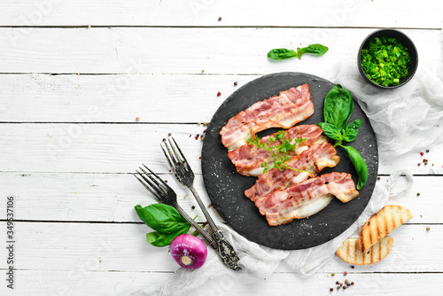 Fried bacon slices with basil on a black stone plate. Top view. Free copy space.