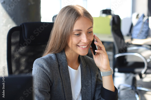 Beautiful business woman is talking on the mobile phone and smiling while sitting in modern office.