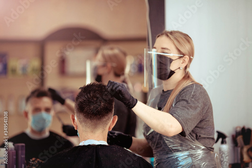 Hairdresser with security measures for Covid-19, cuts a man in a medicine mask, social distance, cutting hair with a medical mask, eye mask and rubber gloves.