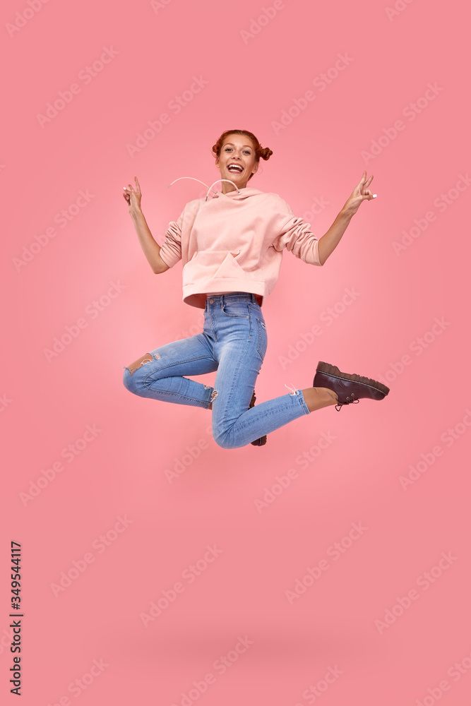 Full length shot of happy cheerful red-haired beautiful young girl in casual clothes jump in air on a pink background. Concept of happy news and promotions for youth. Advertising space Full length shot of happy cheerful red-haired beautiful young girl in casual clothes jump in air on a pink background. Concept of happy news and promotions for youth. Advertising space