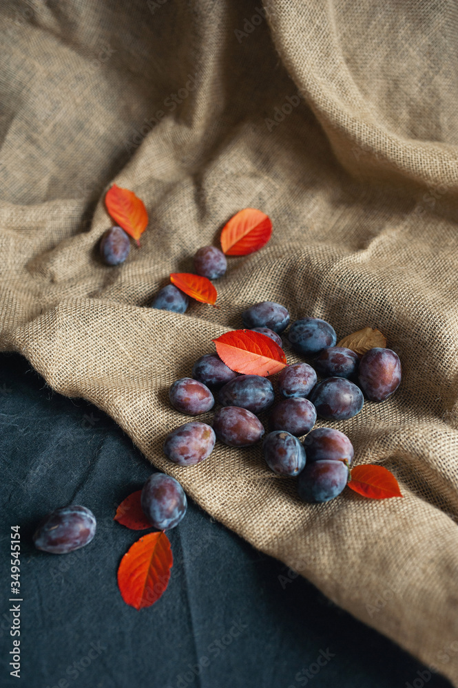 Ripe plums on the table. Decoration with red leaves Ripe plums on the table. Decoration with red leaves