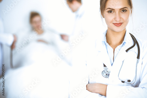 Female doctor smiling on the background with patient in the bed and two doctors