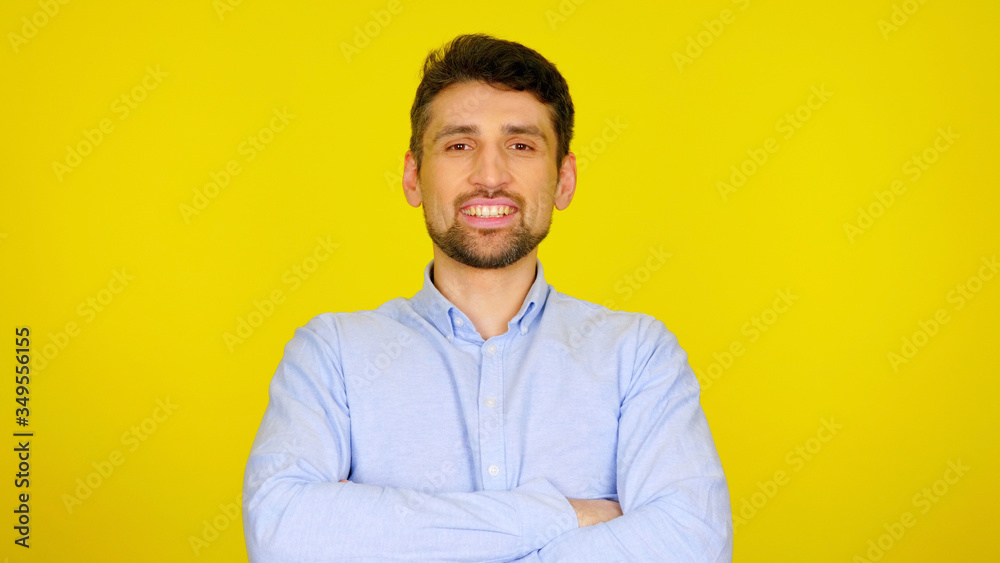 Handsome bearded man in a light blue shirt smiles. Businessman looking at the camera on a yellow background with place for text