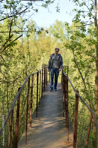 A man walking along a high bridge among branches of bushes and trees