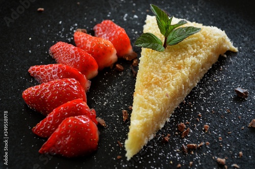 Fresh homemade coconut cake with some sliced strawberries, fresh mint, and coconut sprinkles as a topping on a black background photo