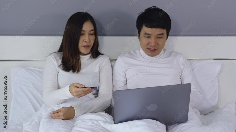 couple using laptop computer to shopping online with credit card on a bed couple using laptop computer to shopping online with credit card on a bed