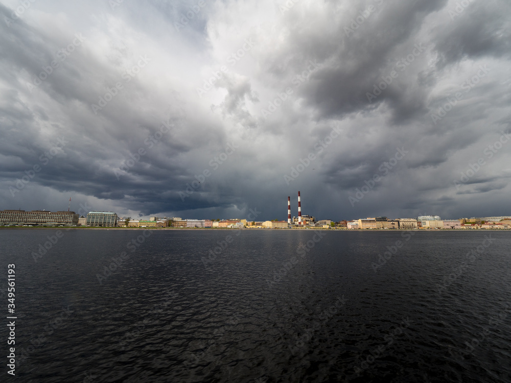 Granite embankment of the river with storm clouds over the water. Spring city landscape with a river.