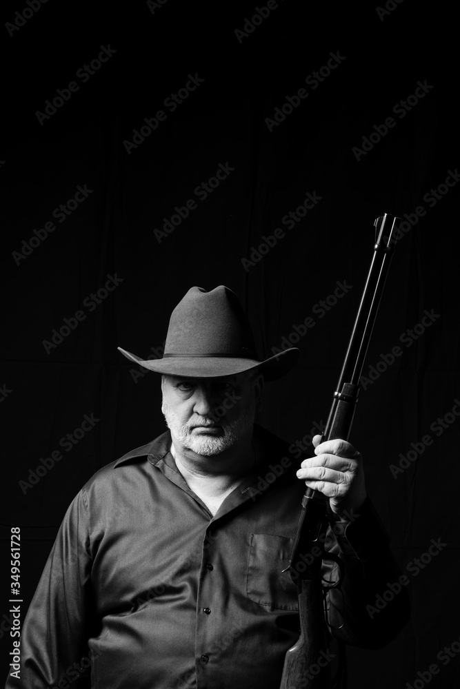 Older man in a cowboy hat with a gray beard holding a lever action rifle with a black background Older man in a cowboy hat with a gray beard holding a lever action rifle with a black background