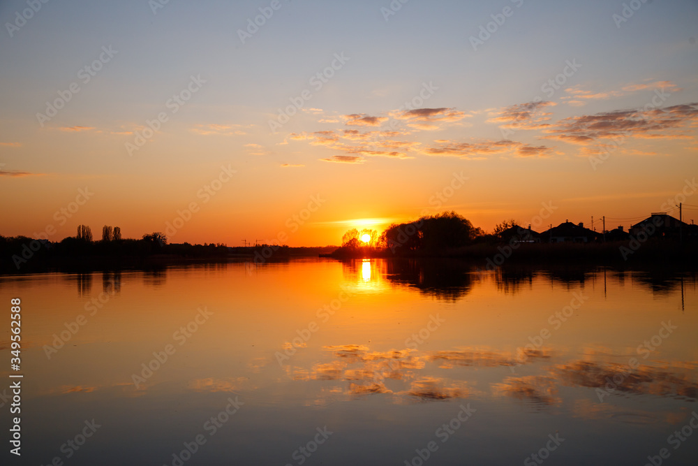 Sunset on the lake, the sun sets behind the trees and beautiful reflections in the water