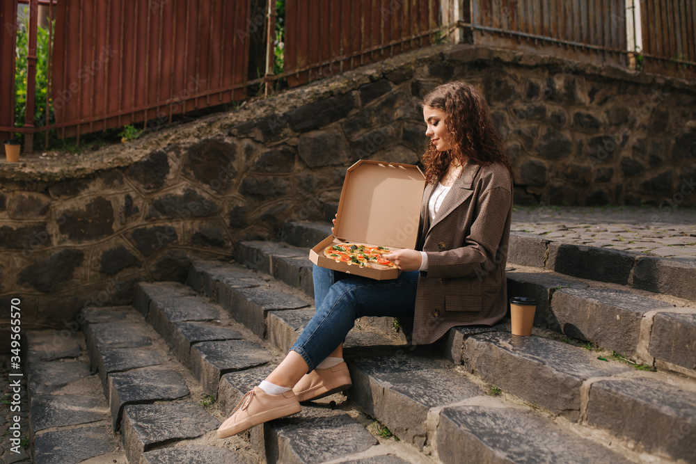 Fototapeta premium Attrative woman open pizza box and eating vegan pizza outdoors
