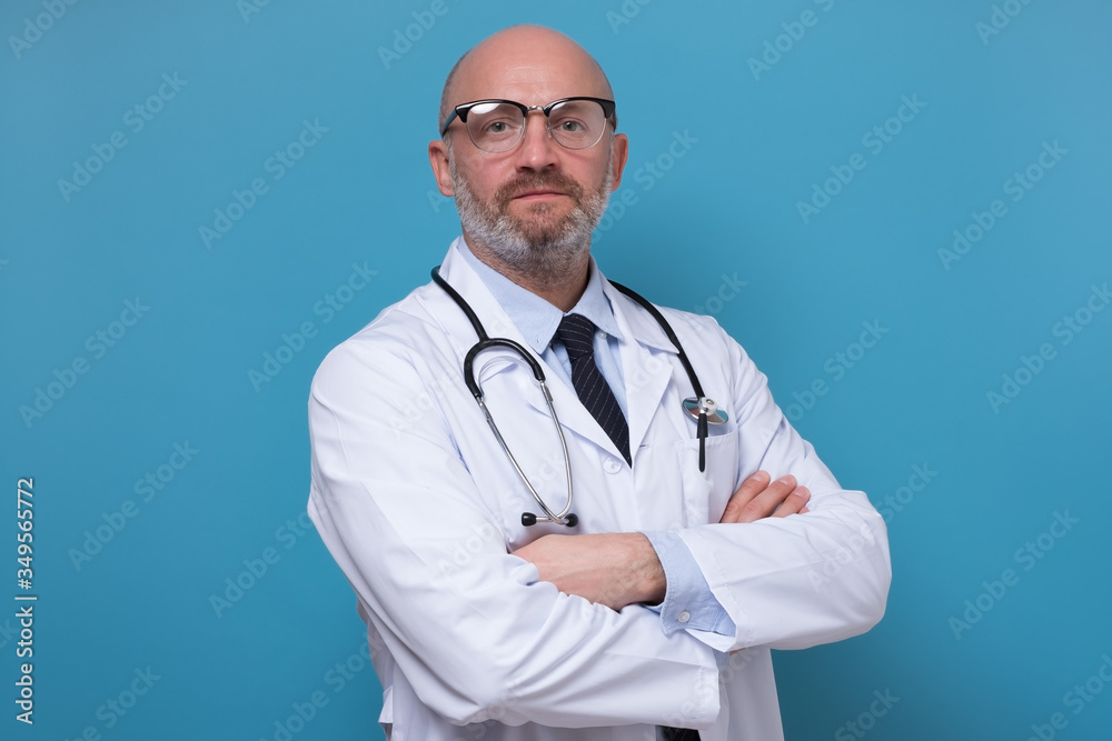 Serious middle aged doctor in labcoat with stethoscope looking at camera. Studio shot on blue wall. Serious middle aged doctor in labcoat with stethoscope looking at camera. Studio shot on blue wall.